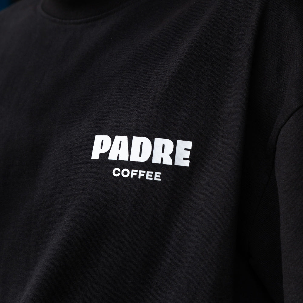 Close-up of a black tee featuring the words 'PADRE COFFEE' printed in bold white capital letters on the chest.