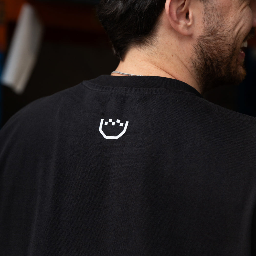 Close-up back view of a man wearing a black t-shirt with a small white stylized logo printed on the upper back.